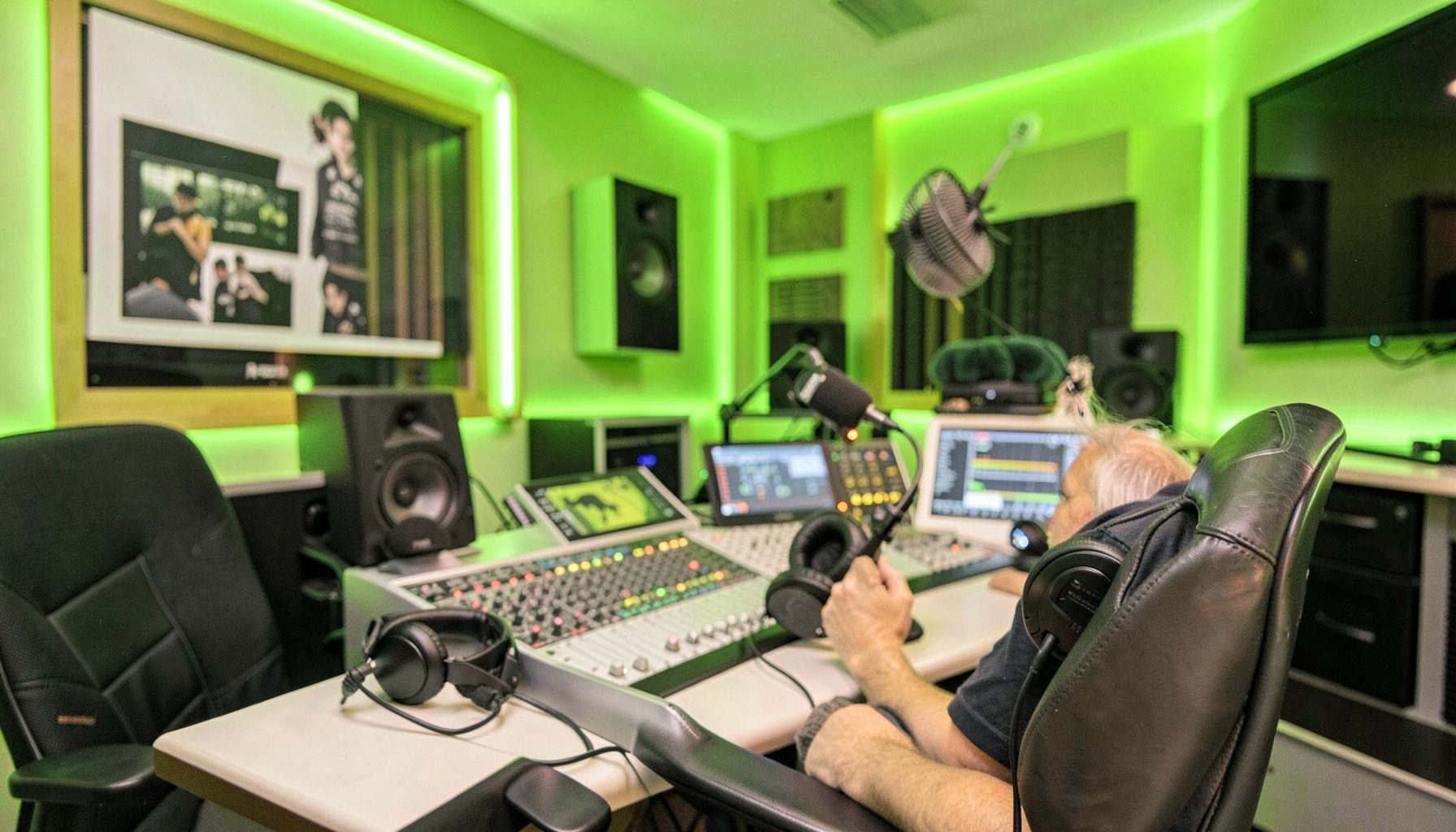 A bright, friendly radio studio interior with lime-green accent lighting, headphones resting on a console, and a relaxed atmosphere